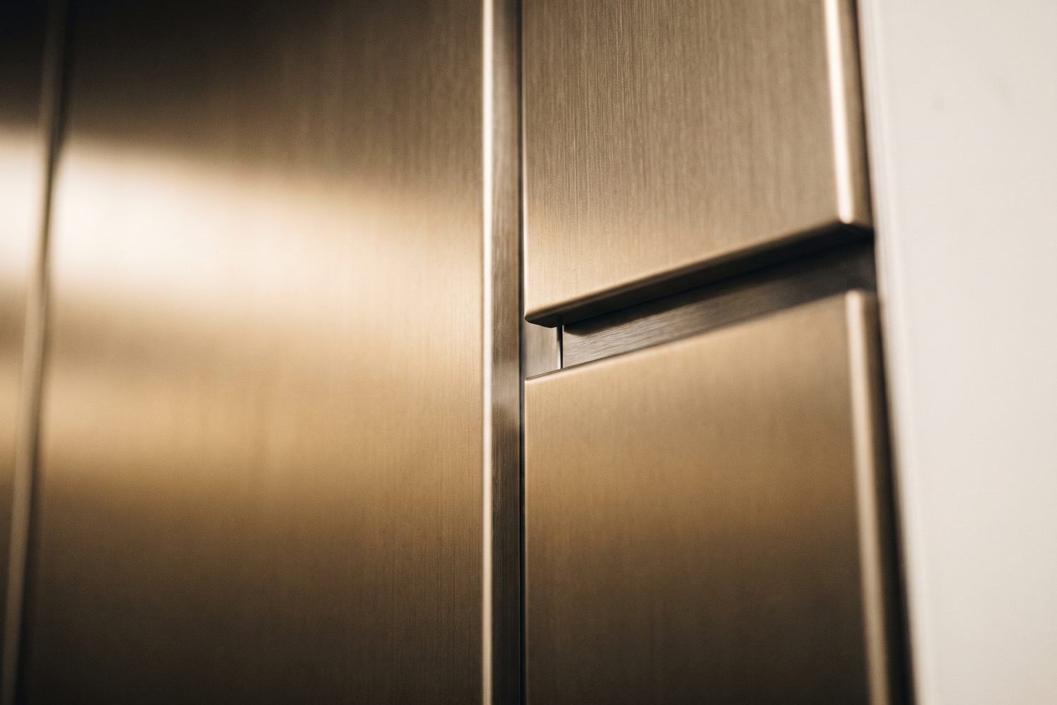 Champagne PVD panel meeting a brushed stainless reveal in a lift